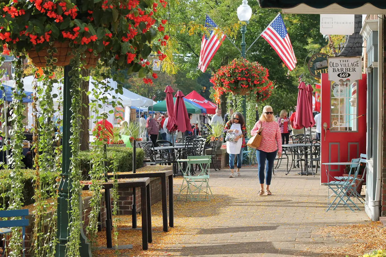 Old Worthington sidewalk in bloom — hanging red flower baskets, American flags, and a red barbershop door