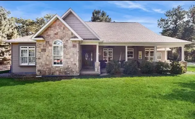 Front view of a suburban house with a stone and siding exterior, front porch, windows, and a well-maintained lawn