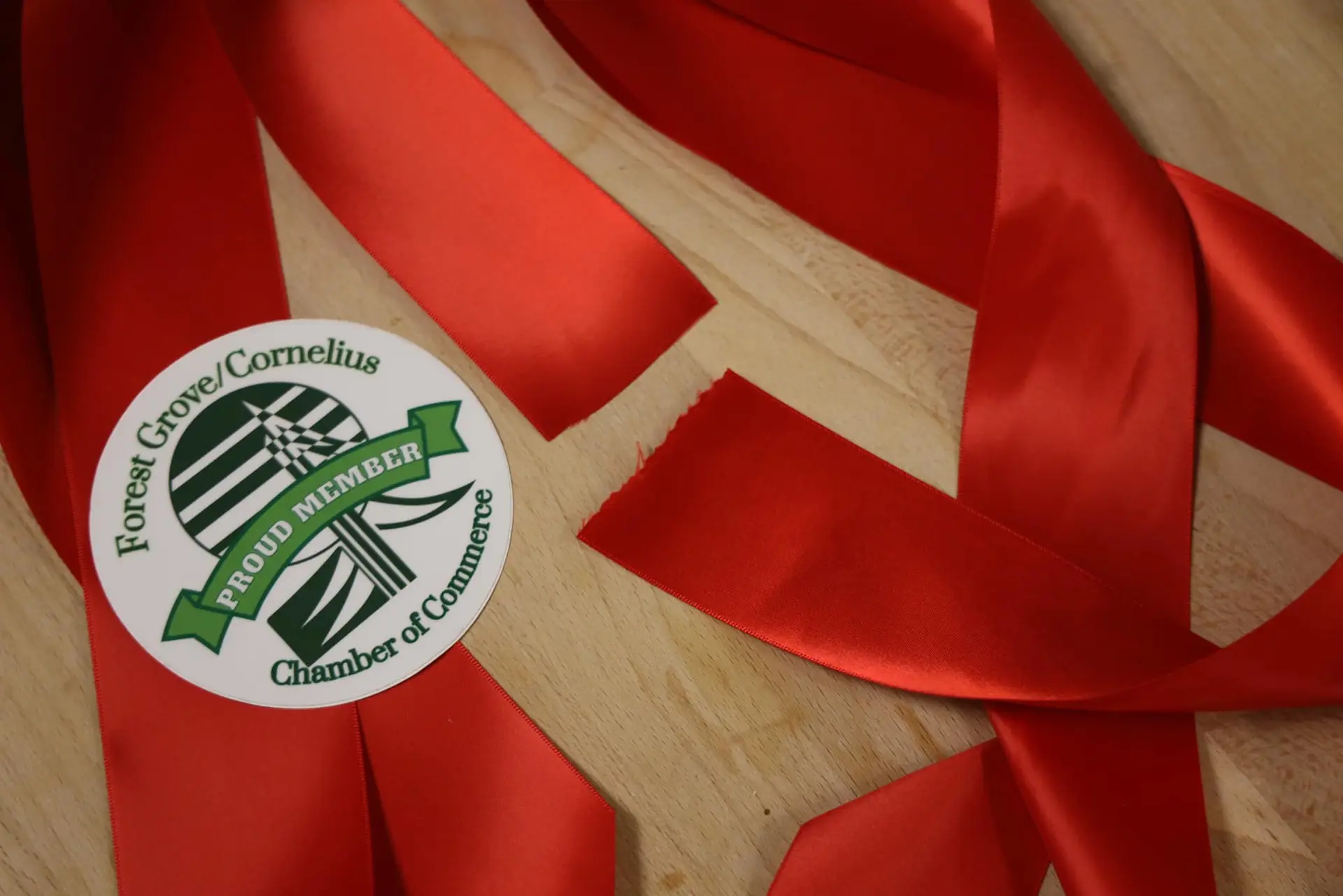 A length of glossy red ribbon coiled on pale wood with a round chamber sticker attached to it.