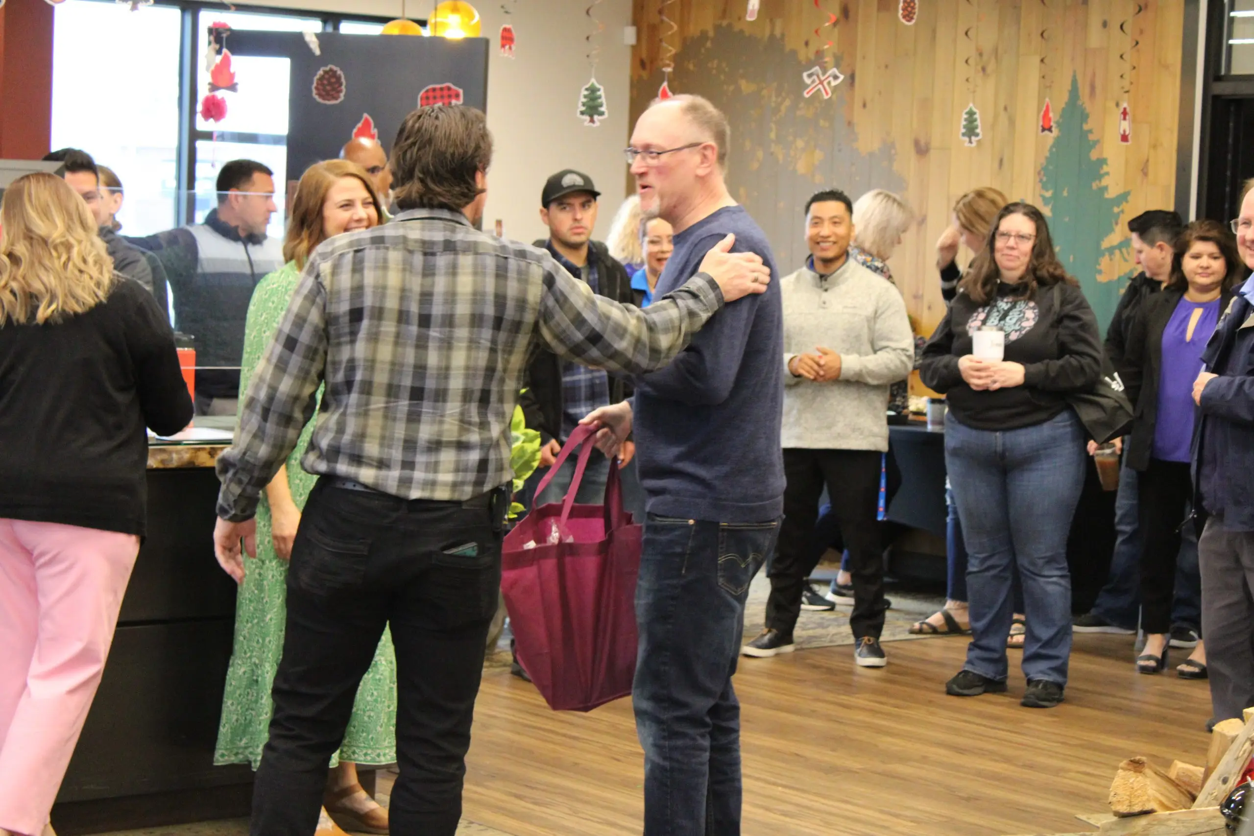 Two men greeting each other with an arm around the shoulder at an indoor chamber event, other guests around them.