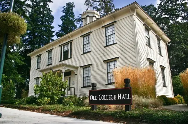 Old College Hall, a white clapboard building with a cupola and tall shuttered windows, with a dark wooden sign reading Old College Hall in front of it.