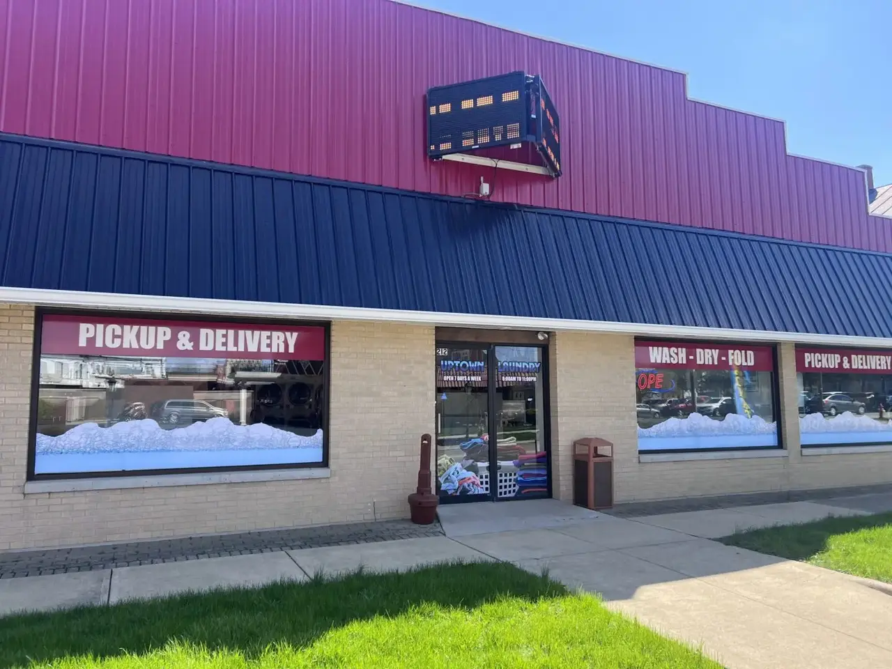 Exterior of Uptown Laundry in Bucyrus, Ohio, showing the storefront with pickup and delivery signage, wash–dry–fold windows, and the main entrance.
