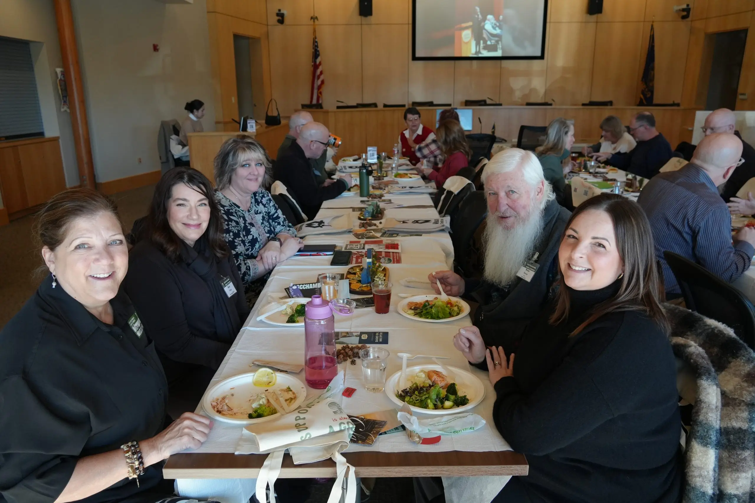 A long banquet table seen down its length with guests seated on both sides, several turning to smile at the camera.