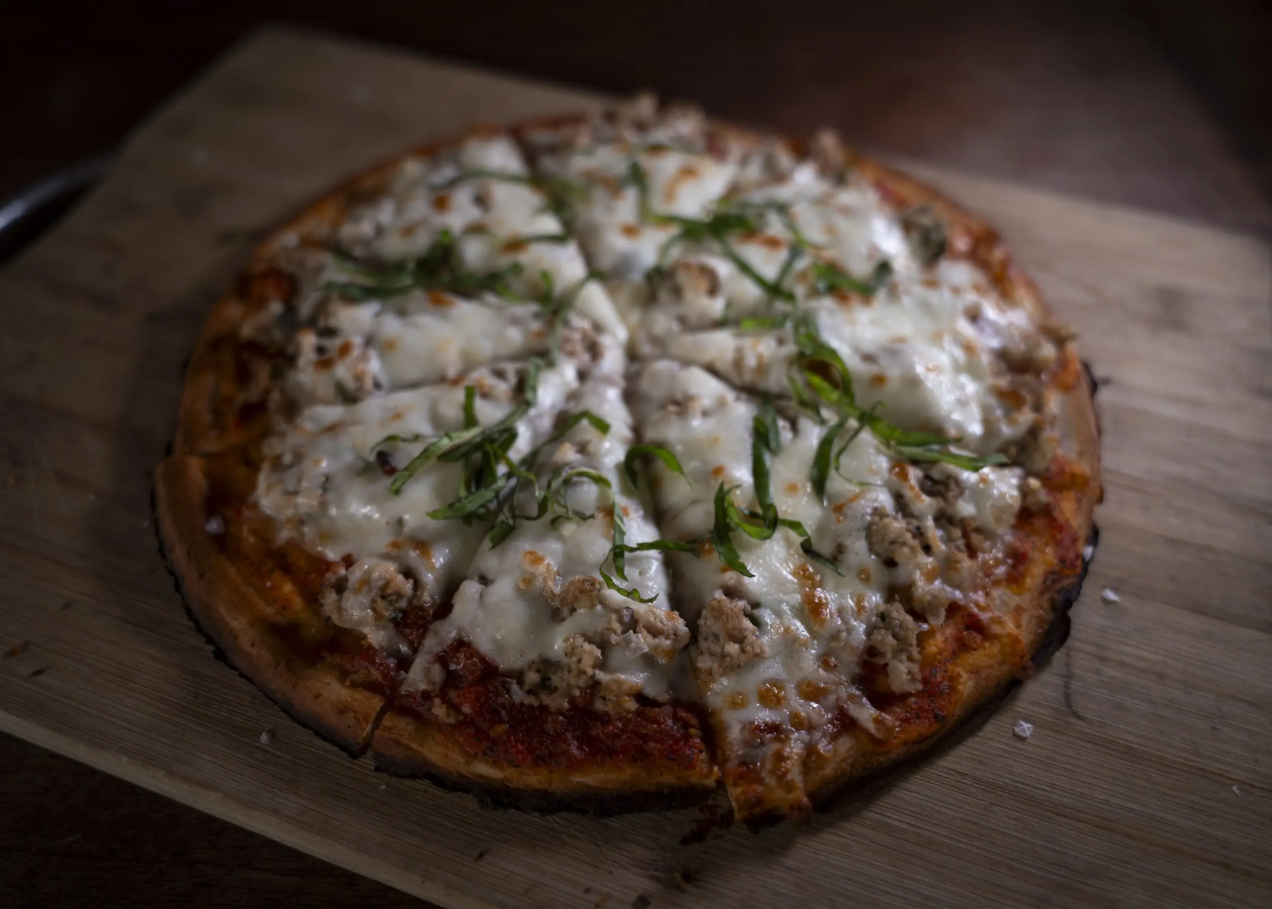 A whole pizza with melted cheese and fresh basil on a dark wooden board.