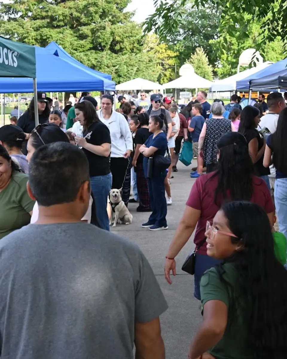 Crowd of community members walking among vendor booths at an outdoor community event.