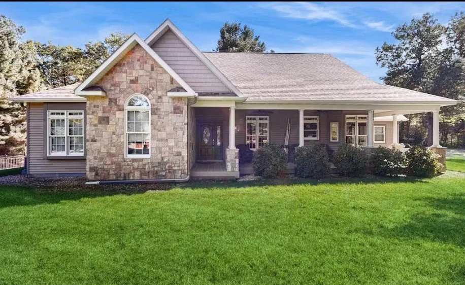 Front view of a suburban house with a stone and siding exterior, front porch, windows, and a well-maintained lawn