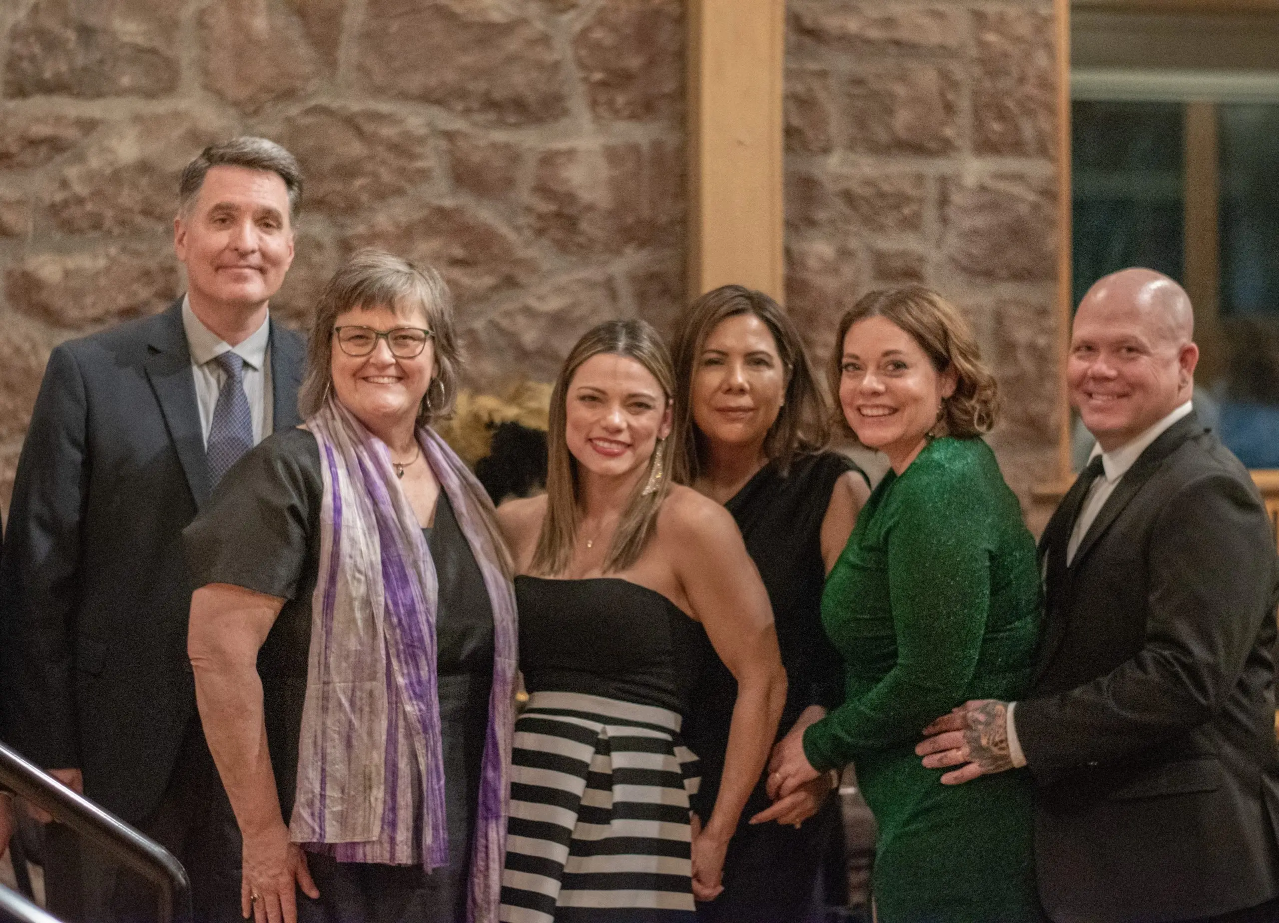 Six people posed together at the gala against a pink stone wall.
