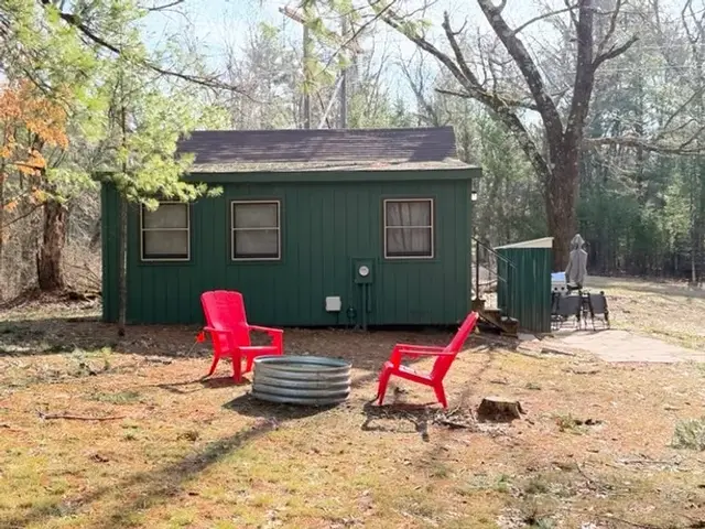 A cozy little dark green cabin in the woods, with a setting for a campfire outside
