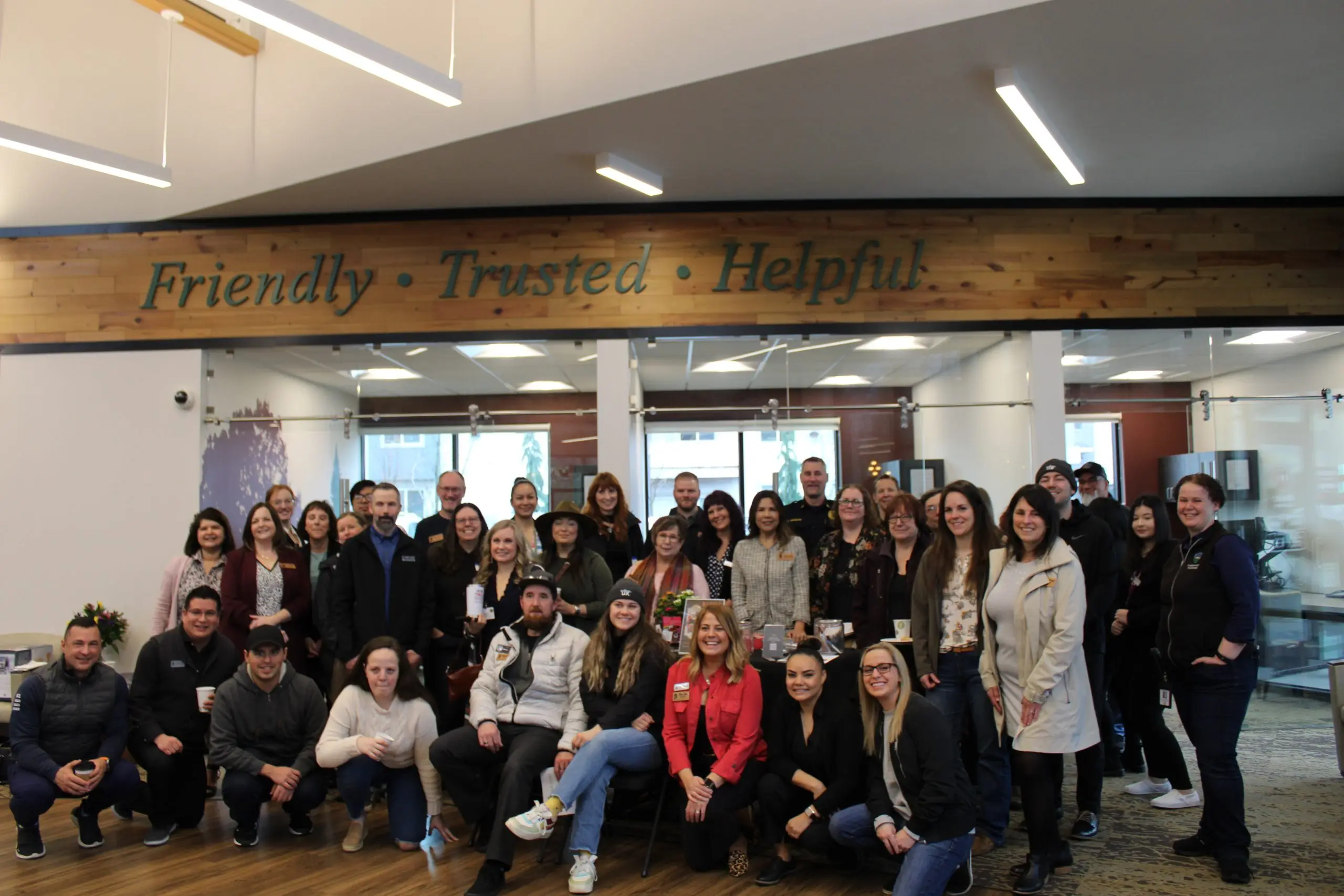 A large group of chamber members standing and kneeling together in a bright open lobby under a timber beam.