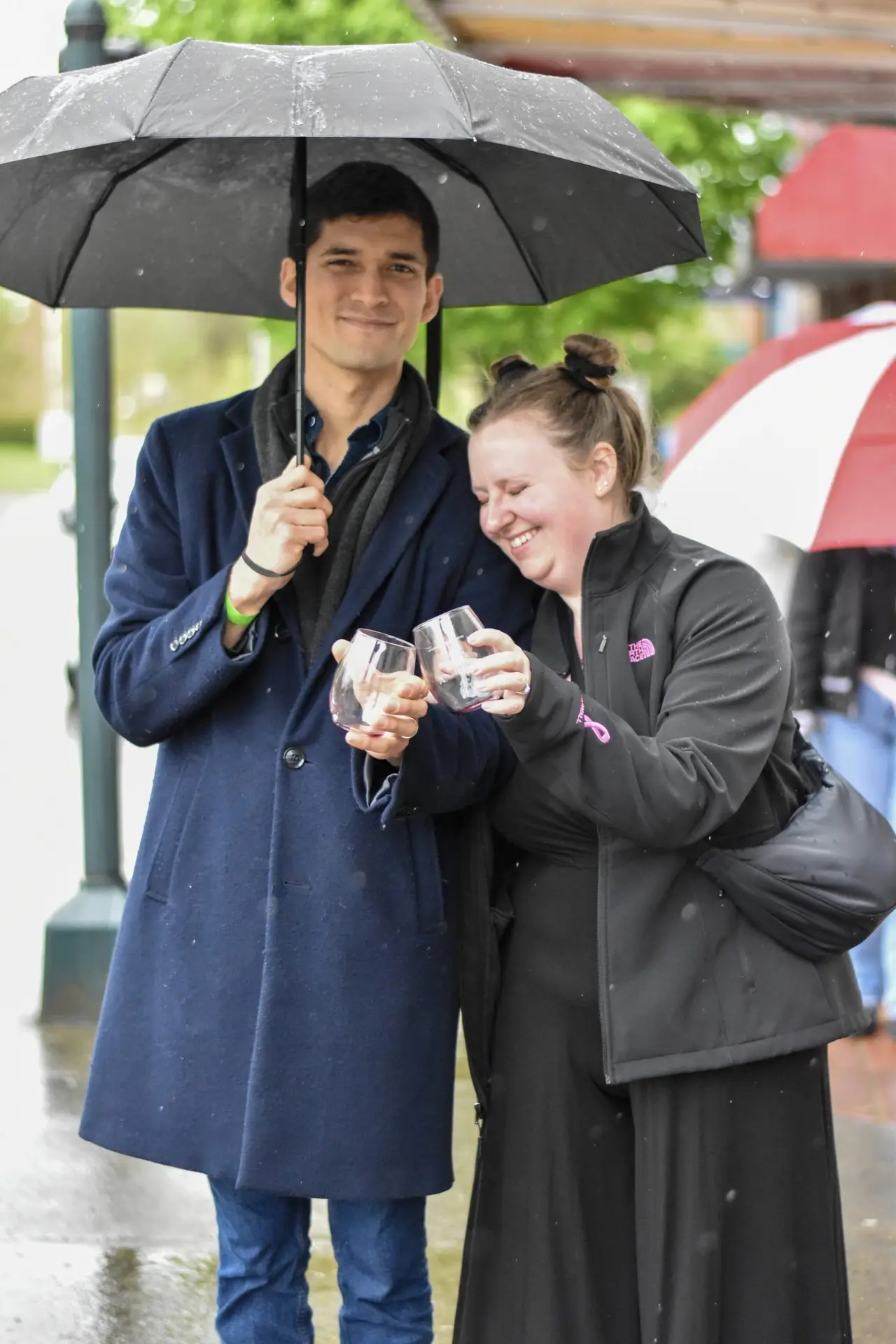 A young man holding a large black umbrella over a laughing woman on a wet downtown street.